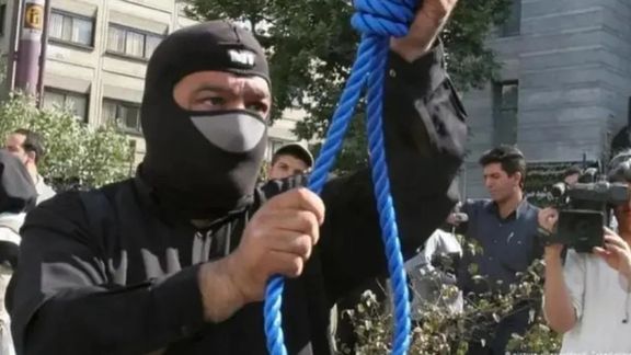 A masked executioner prepares a noose for a public hanging in Iran