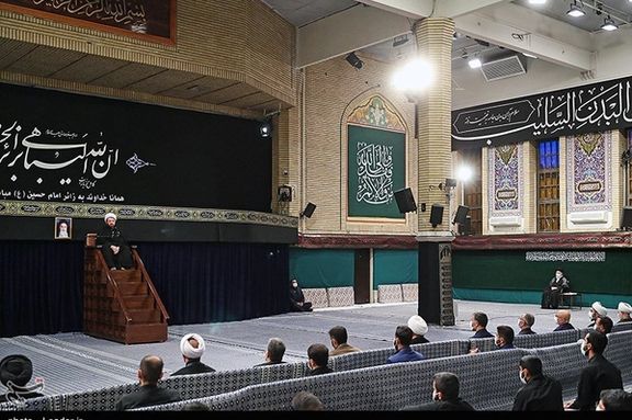 Khamenei sitting to the far right of the hall as a preacher speaks at the traditional manbar