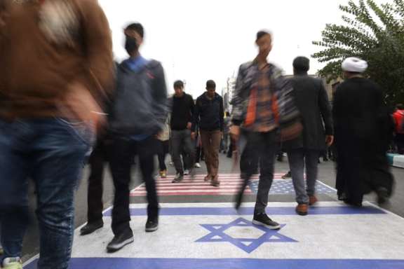 A group of Iranians walk over the flags of Israel and the US during a government-sponsored rally in Tehran