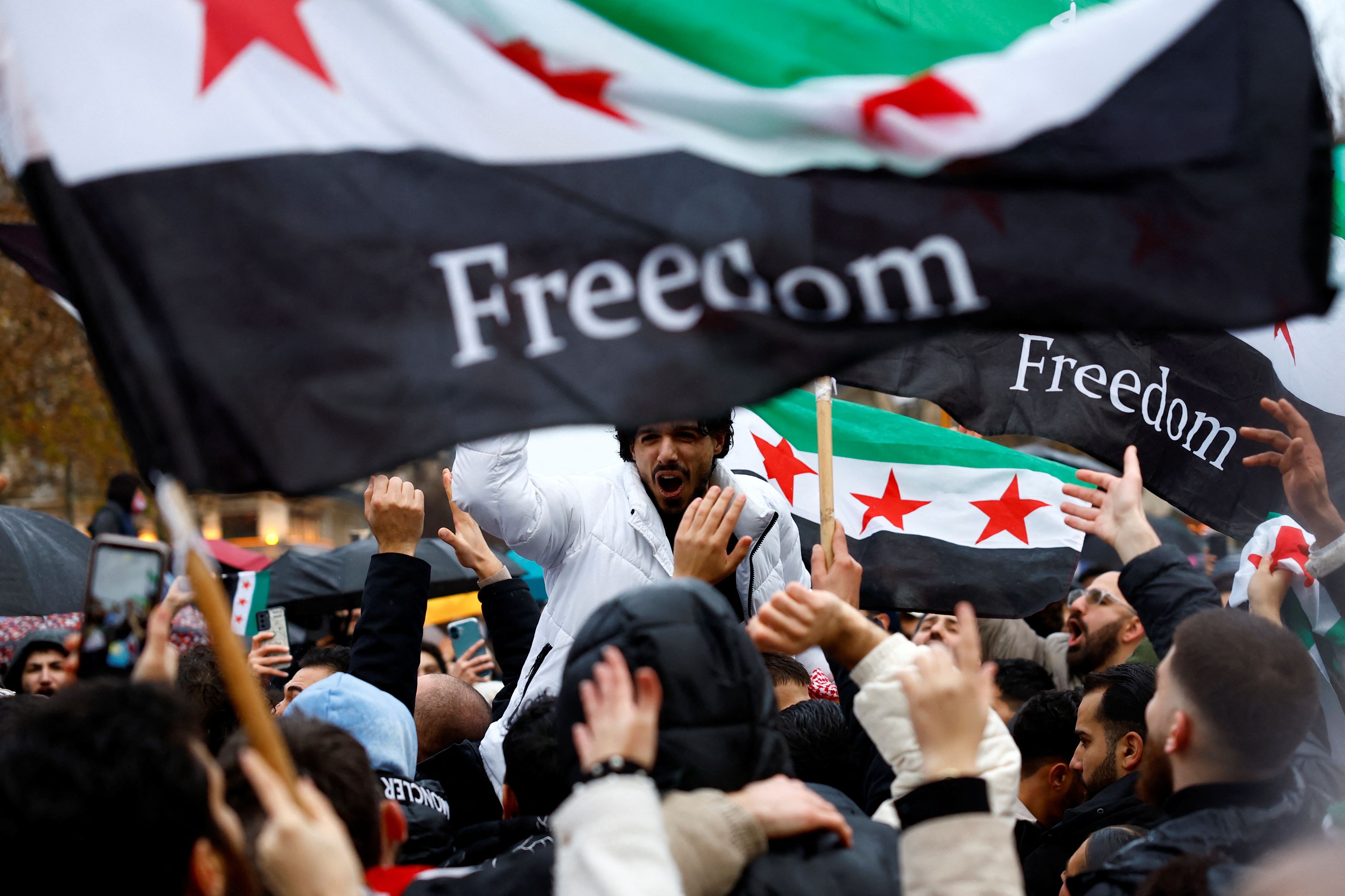 People hold Syrian opposition flags as they celebrate at the Place de la Republique, after Syrian rebels announced that they have ousted President Bashar al-Assad, in Paris, France, December 8, 2024. 