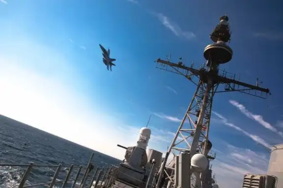 A US Navy F/A-18E Super Hornet fighter jet flies over the guided-missile cruiser USS Philippine Sea in December 2023