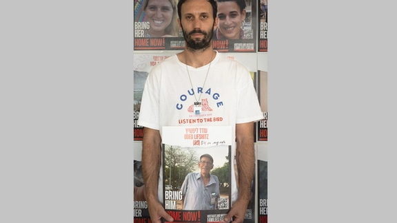 Daniel Lifshitz holding a photo of his grandfather Oded Lifshitz, still a hostage in Gaza.