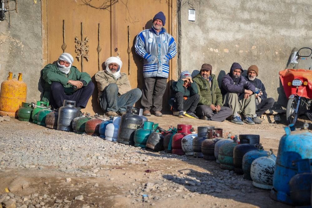 People wait beside gas cylinders during a gas outage in Torbat-e Jam, northeastern Iran, on January 16, 2026.