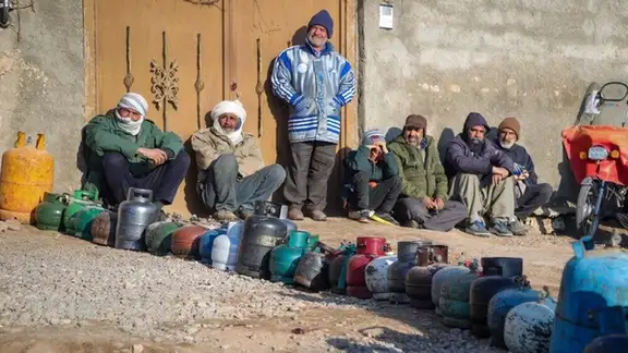 People wait beside gas cylinders during a gas outage in Torbat-e Jam, northeastern Iran, on January 16, 2026.