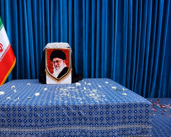 Potret Pemimpin Tertinggi Iran, Ali Khamenei, dipajang di atas mimbar upacara yang dilapisi kain hitam dan dihiasi dengan spanduk duka.