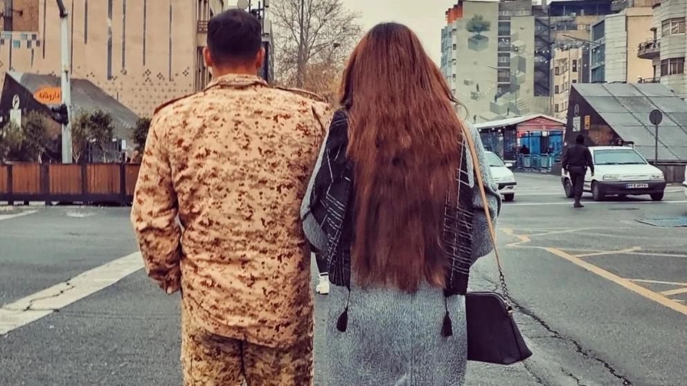 A woman defying Iran's hijab regulations walks alongside a conscript in Tehran's Valiasr crossroad in December 2024