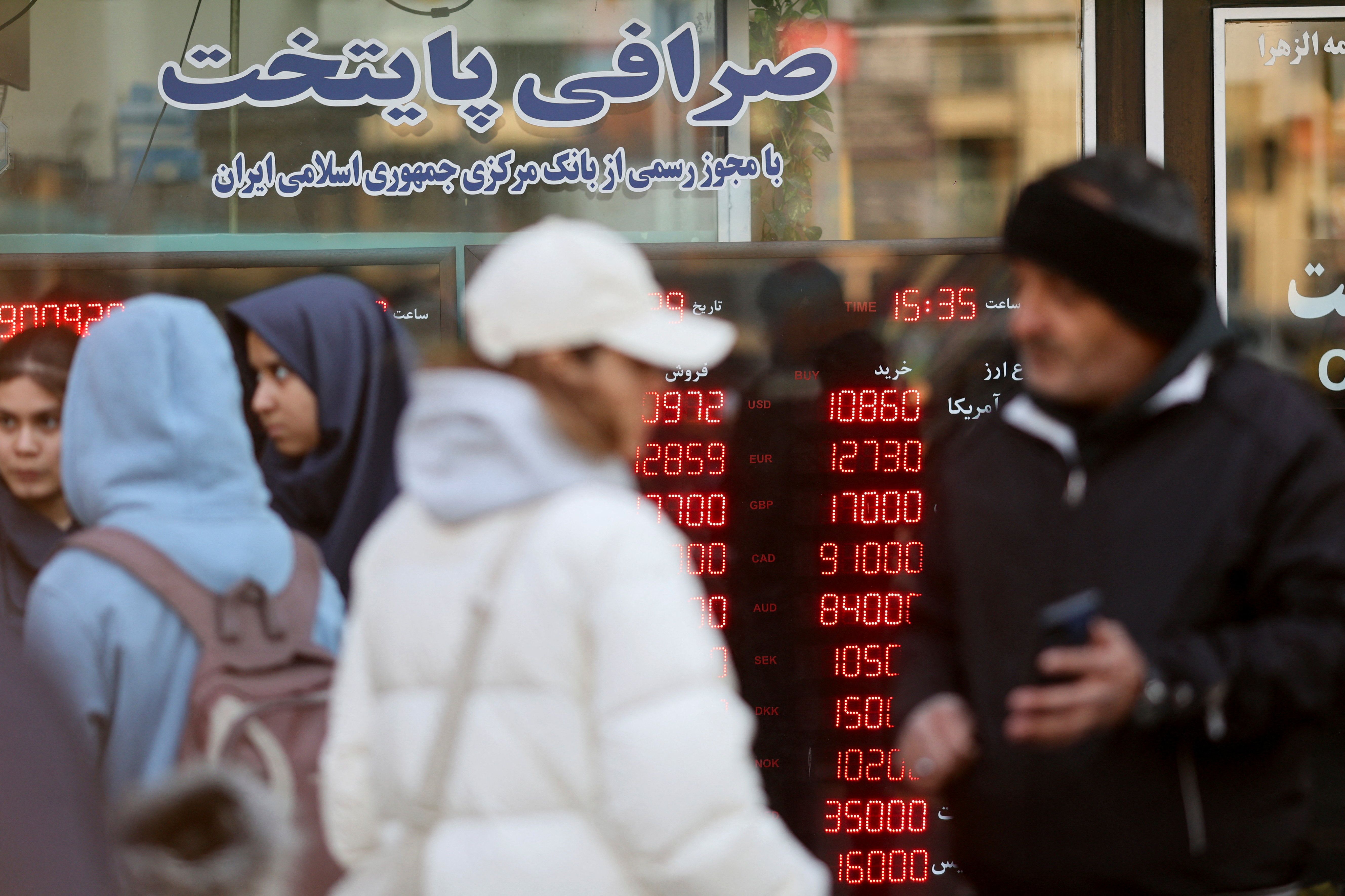People walk past a display sign at a currency exchange bureau as the value of the Iranian rial drops, in Tehran, Iran, December 20, 2025.