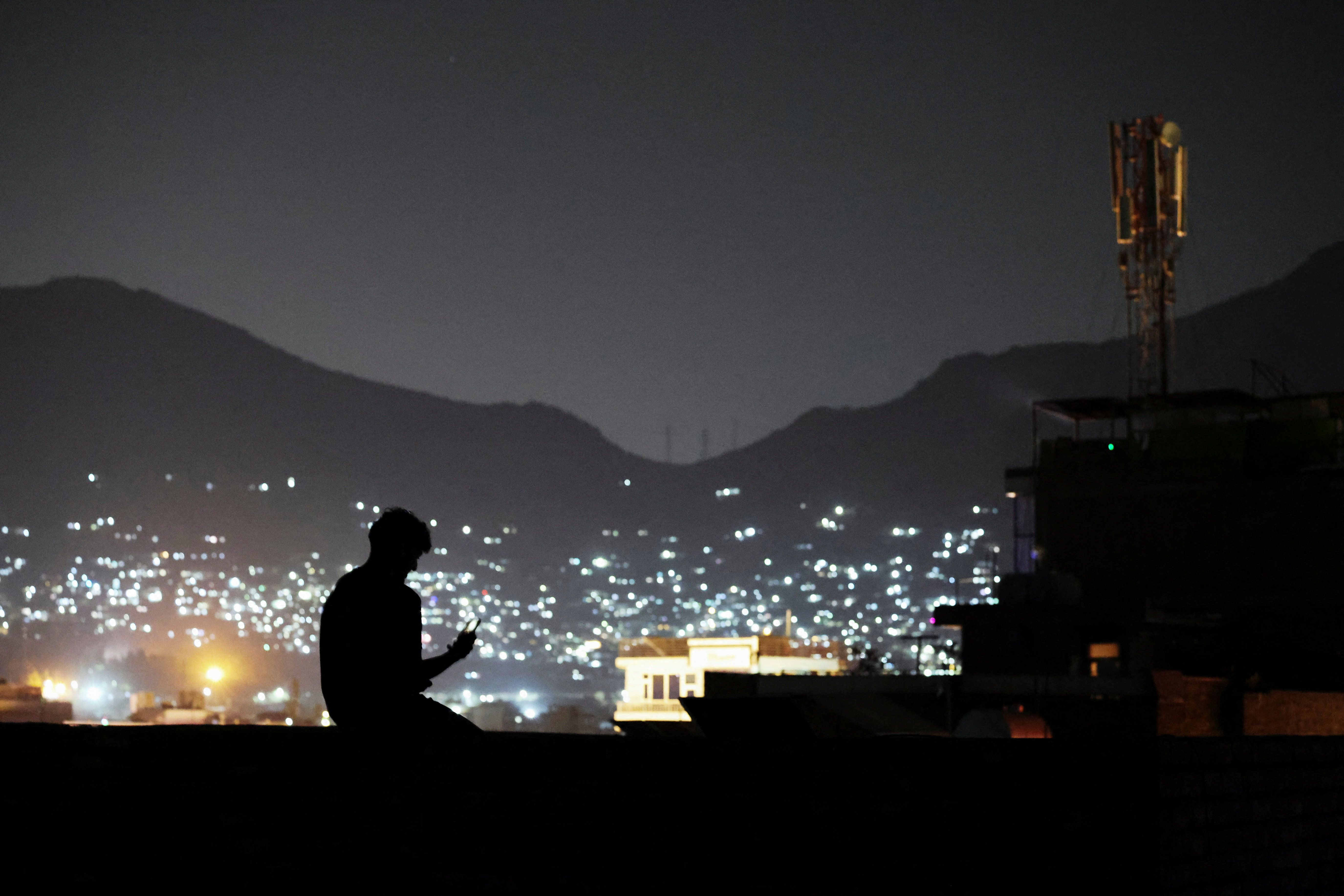 Silhouette of a man using a mobile phone during a nighttime internet blackout in Iran amid ongoing restrictions and connectivity disruptions.