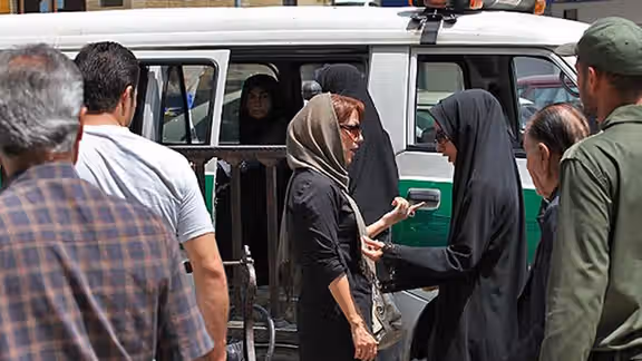 A woman with a headscarf showing part of her hair being questioned by 'chastity police' in Iran equipeed with a special van to detain women. June 2022