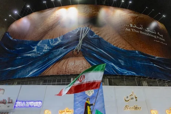 A woman waves an Iranian flag beneath a giant anti-US billboard depicting, in a state-backed rally in Tehran, May 9, 2026