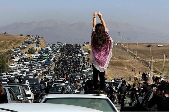 A woman stands on top of a car as protesters make their way toward the cemetery where Mahsa Amini is buried.