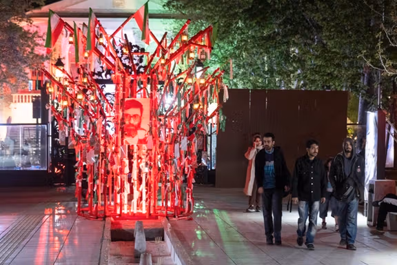 People walk past a religious symbol with a portrait of Iran's slain Supreme Leader Ali Khamenei in northern Tehran on April 12, 2026.