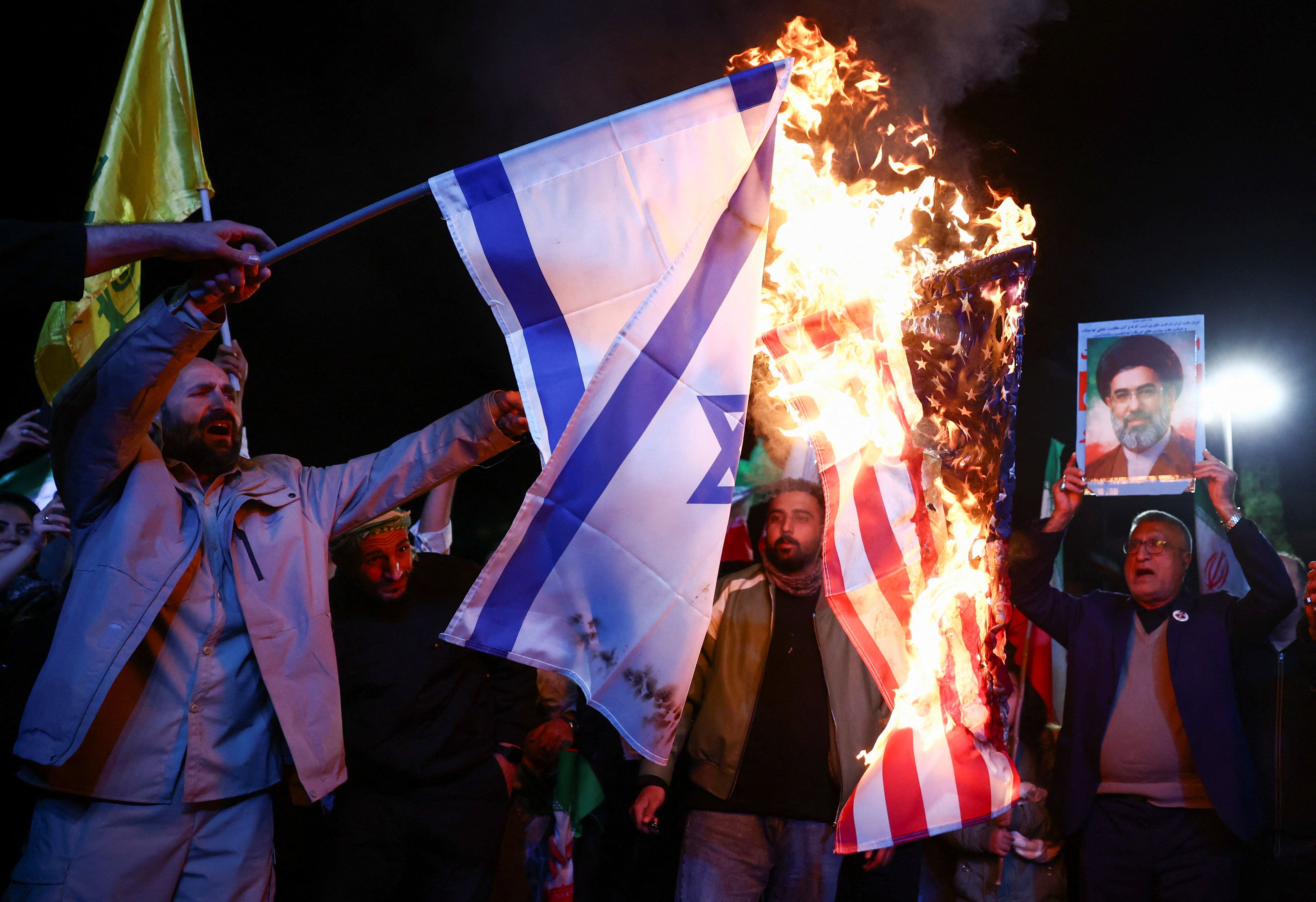 A man holds a photo of Iran's Supreme Leader, Mojtaba Khamenei, while the flags of the US and Israel are burnt, as people gather after a two-week ceasefire in the Iran war was announced, in Tehran, Iran, April 8, 2026. 