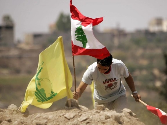 A Lebanese man plants a national flag in the ground at a cemetery before a funeral ceremony for the victims of the conflict between Israel and Lebanon's Hezbollah in the city of Qana.