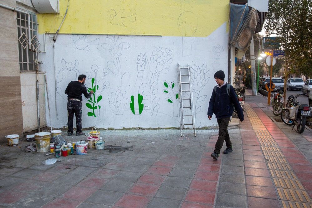 A pedestrian passes as an artist paints a mural on a wall in the Chaharmardan neighborhood of Qom, central Iran.