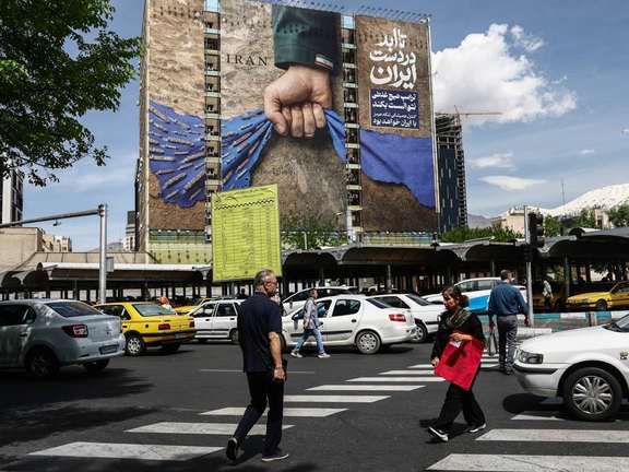 People walk at a busy street with a large billboard depicting Iran's 'control' over the Strait of Hormuz, Tehran, April 27, 2026