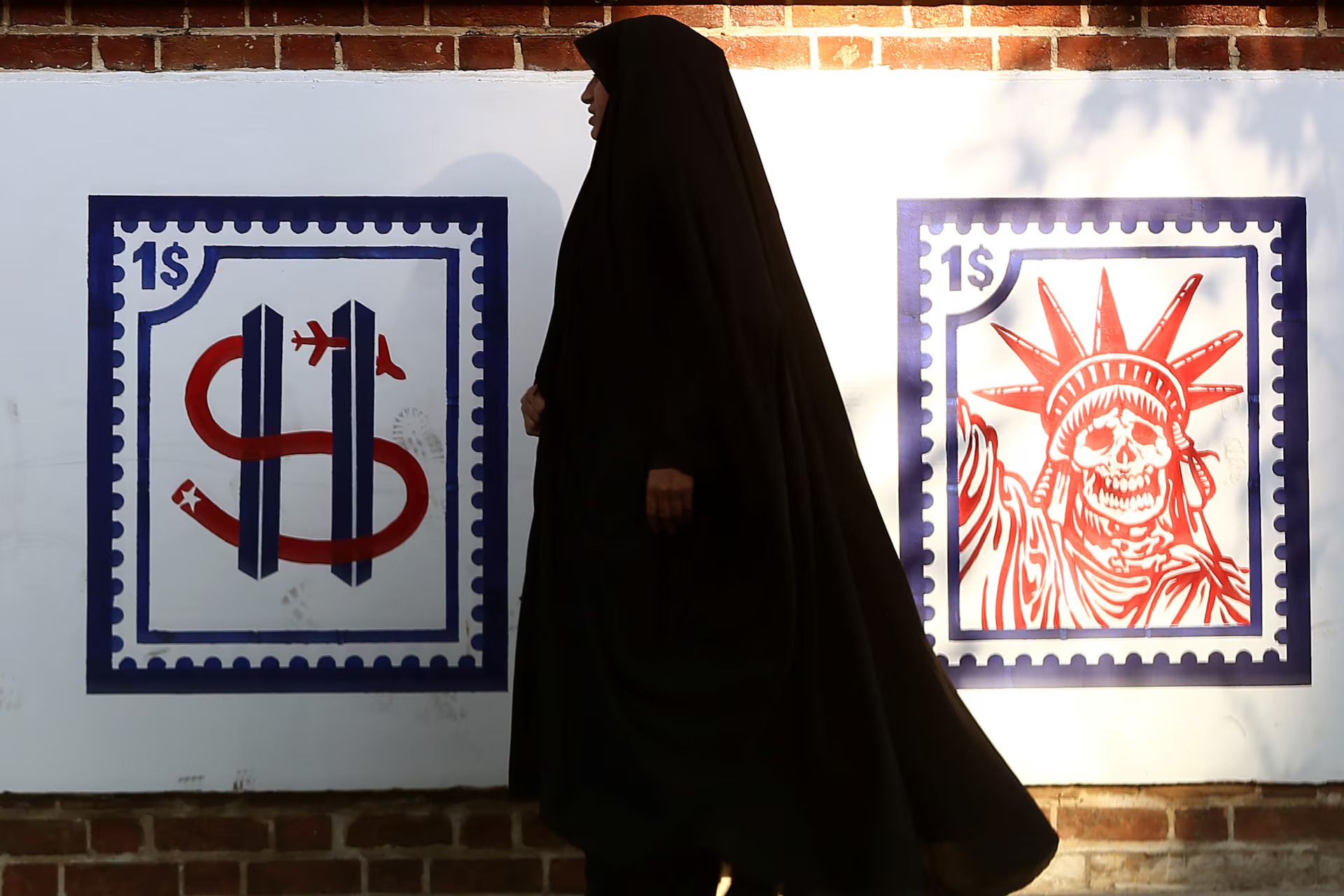 A woman walks past an anti-US mural on the former U.S. embassy's wall in Tehran, January 03, 2020.