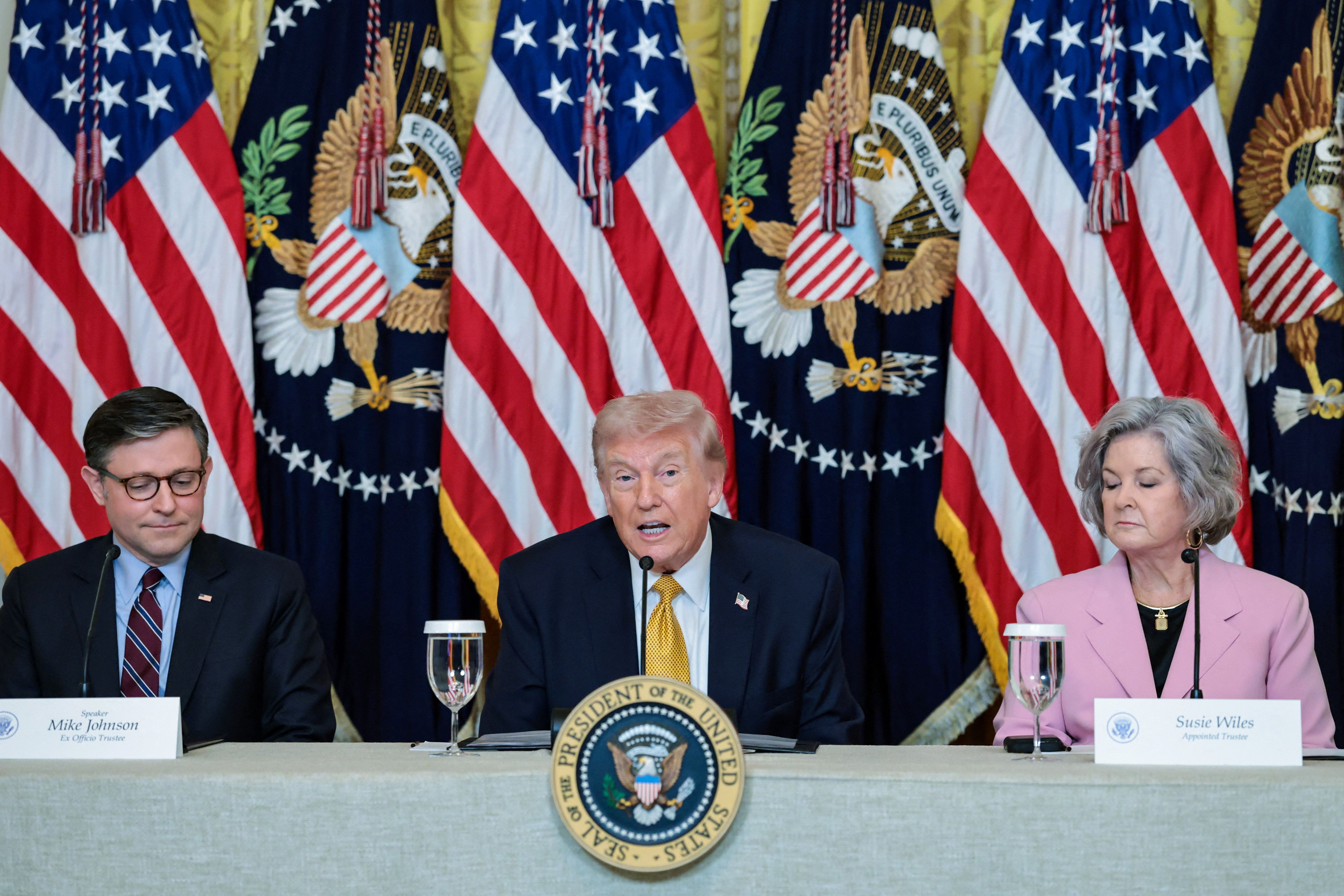 President Donald Trump, flanked by the Speaker of the House Mike Johnson (R-LA) and White House chief of staff Susie Wiles, speaks during a lunch with the Kennedy Center board members in the East Room of the White House in Washington, D.C., U.S., March 16, 2026. 