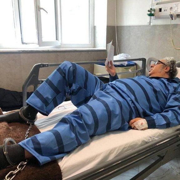 بکتاش آبتین روی تخت بیمارستان با لباس زندان و پاهای بسته به زنجیر