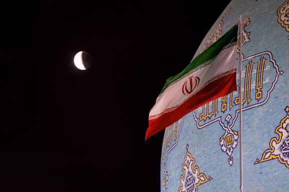 An Iranian flag flies next to a mosque in Qom during a lunar eclipse, September 7, 2025