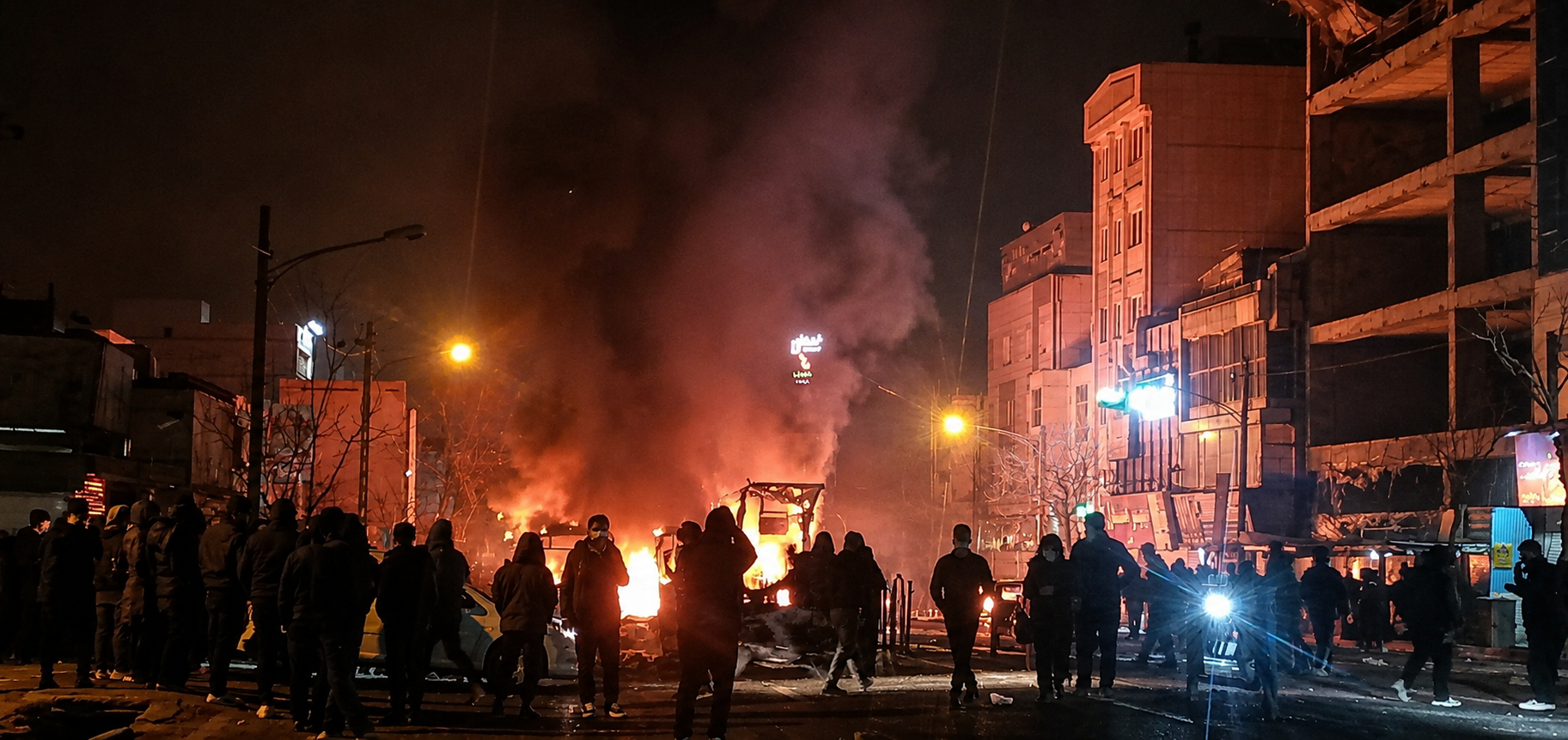 People gather around burning debris on a street in Iran in during January 2026 protests.