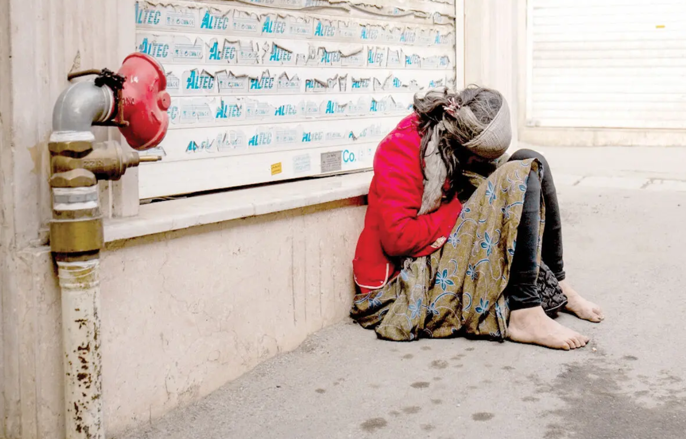 A woman with drug addiction sits on a pavement in Tehran in an undated image.