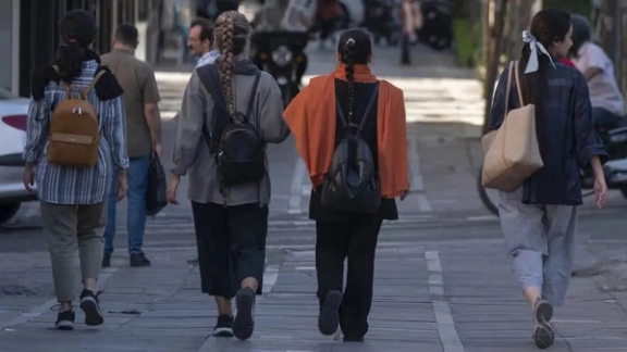 Women walk along a city street in Iran as their head coverings loosely draped