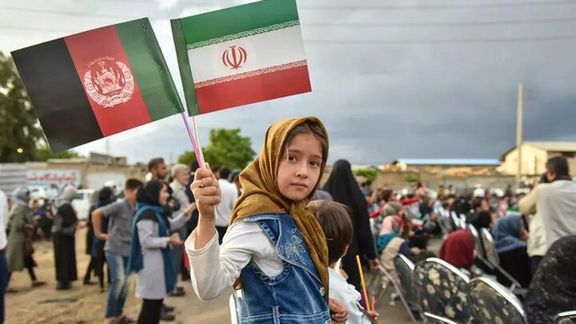 An Afghan girl holding the flags of the Islamic Republic of Iran and Afghanistan