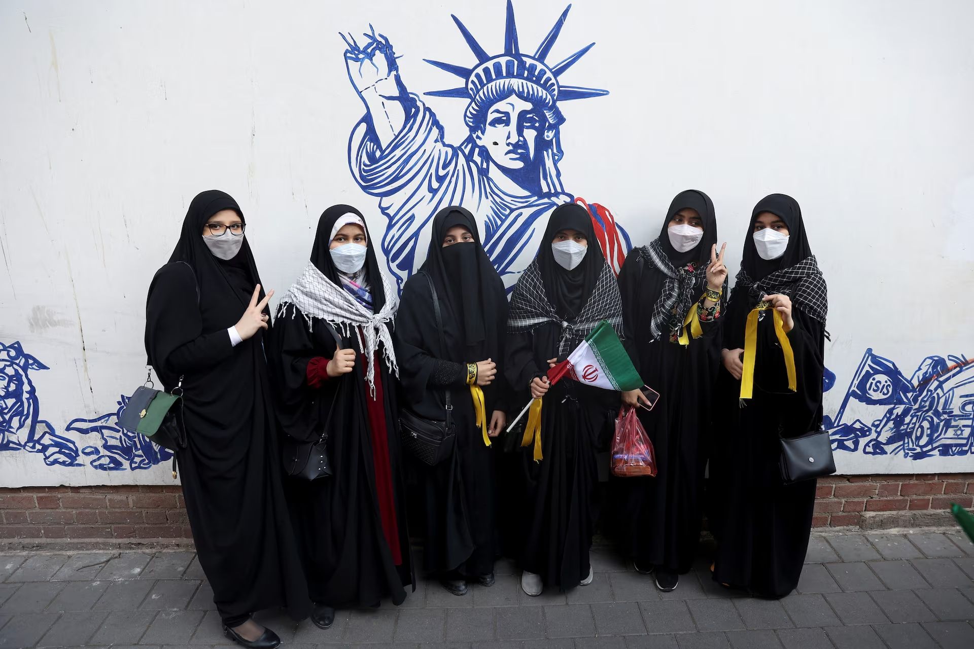 Demonstrators stand in front of a wall of the former US embassy with anti-US murals on the 42nd anniversary of the takeover of the embassy and the US expulsion from Iran, in Tehran, November 4, 2021. 