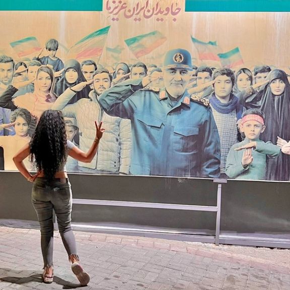 An Iranian woman without mandatory hijab showing a victory sign in front of a mural of Revolutionary Guards Quds force commander Qasem Soleimani