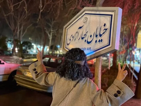 An Iranian woman unveiling in public in front of a street sign that reads “the spring of freedom street” in Tehran