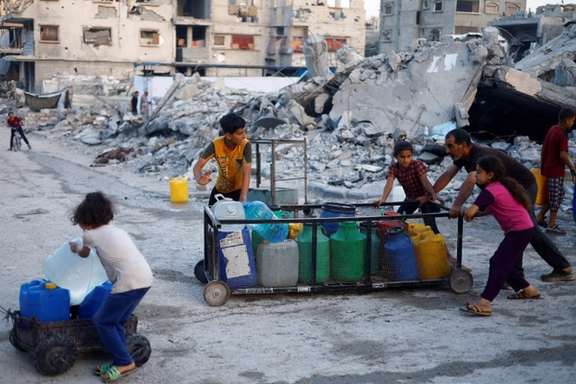 یک مرد و چند کودکان فلسطینی در حال حمل ظروف آب در شهر غزه، ۱۴ خرداد