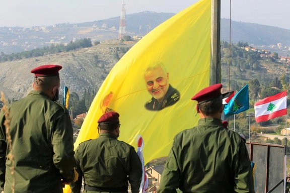 Members of Lebanon's Hezbollah stand near a flag with a picture of slain Iranian commander Qassem Soleimani, during a ceremony marking the first anniversary of the killing of Soleimani and Iraqi militia commander Abu Mahdi al-Muhandis in a US attack, in a southern Lebanese village