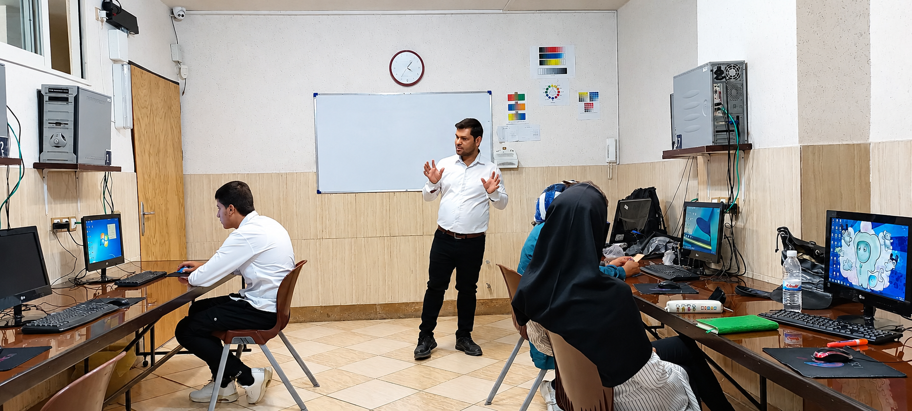 An instructor leads a computer training session in an Iranian classroom as students work at desktop computers.