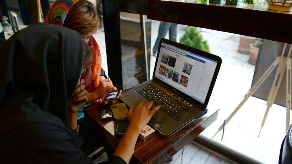 Two women in Iran use a laptop and smartphone in a café to access social media.