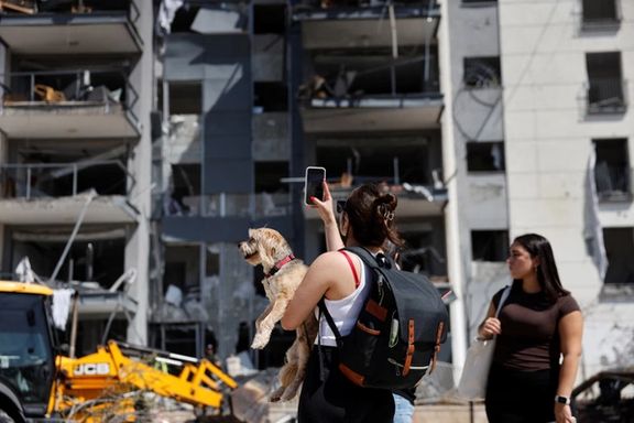 A woman holding a dog takes a photo of a damaged residential building at an impact site following Iran's missile strike on Israel, in Be'er Sheva, Israel, June 20, 2025.