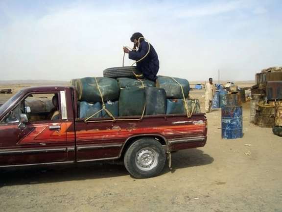A man sits on top of plastic canisters of petrol that he says was brought from Iran, as he prepares to unload them from a van at a roadside shop near a Pakistan and Iran border February 20, 2013.