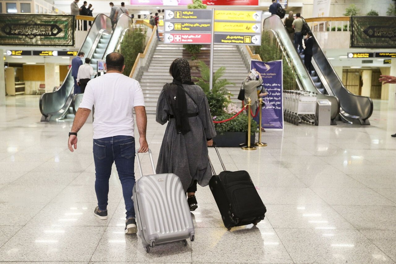 Travelers walk with their luggage inside an airport departure terminal in Iran.