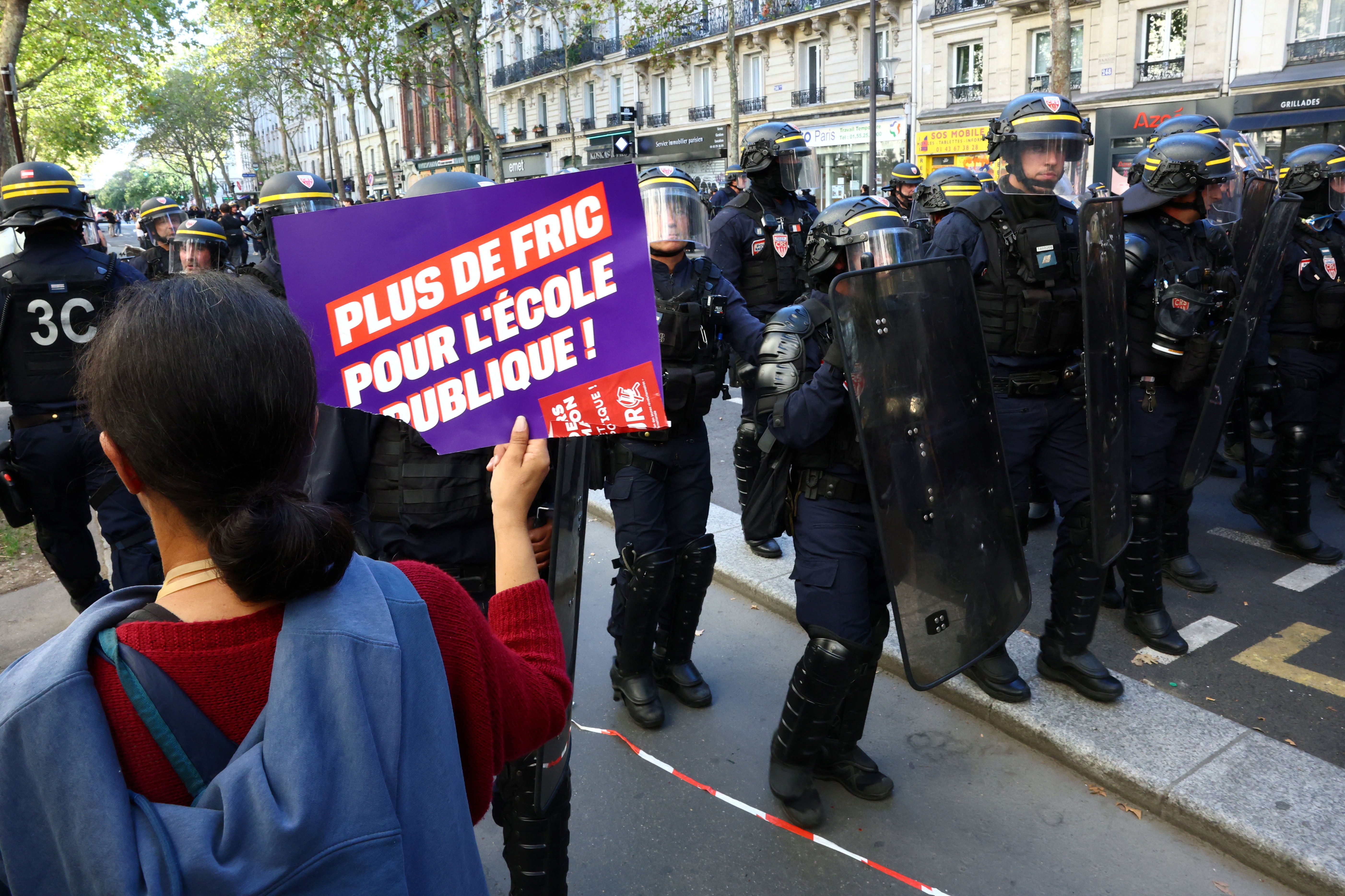 A protester holds a placard reading "More money for public schools" towards French CRS riot police who stand in position during a demonstration by high school and university students.